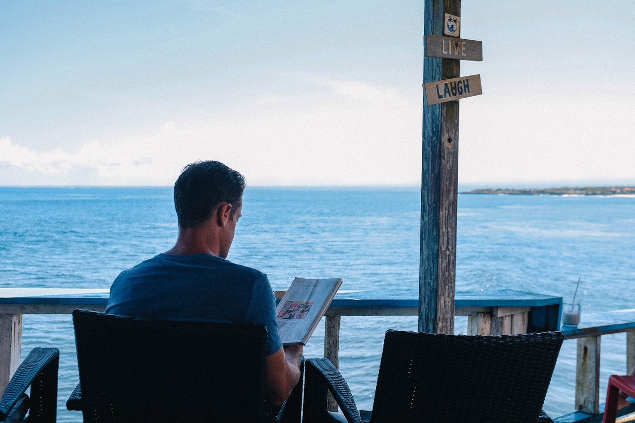 man reading the best books about sailing and sailing books while sitting on a pier overlooking the water